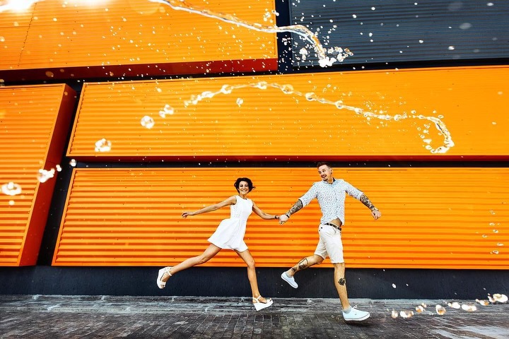 Couple moving in front of bright orange shutters with water droplets overhead