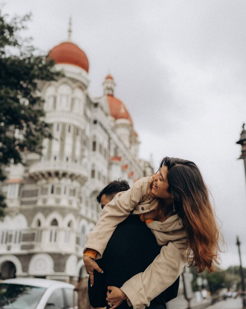 Couple laughing in a piggyback portrait beside a city street and domed building
