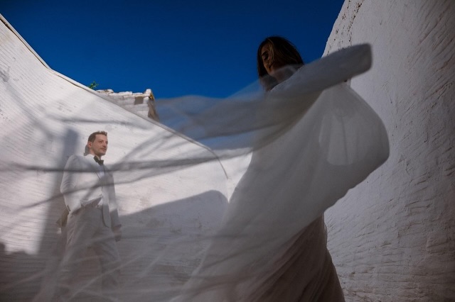 Bride seen through white fabric billowing against a blue sky