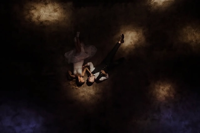 Couple photographed from above on dark ground with patches of warm light