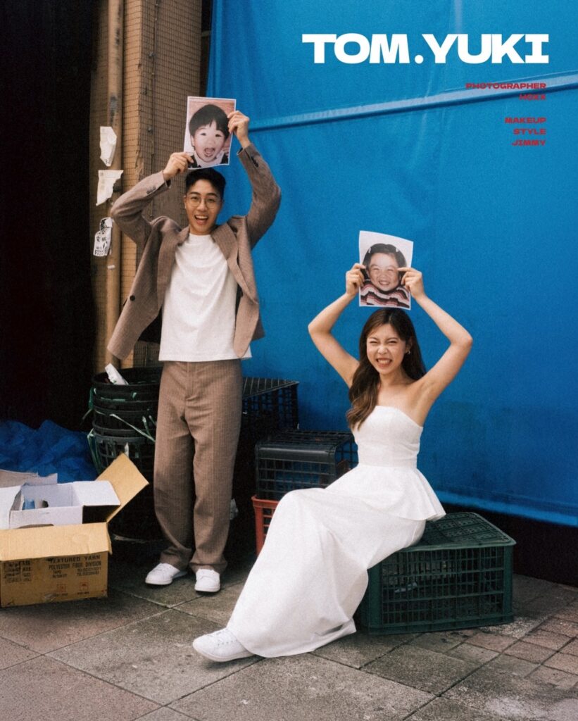 Wedding couple holding printed faces above their heads beside a blue vehicle