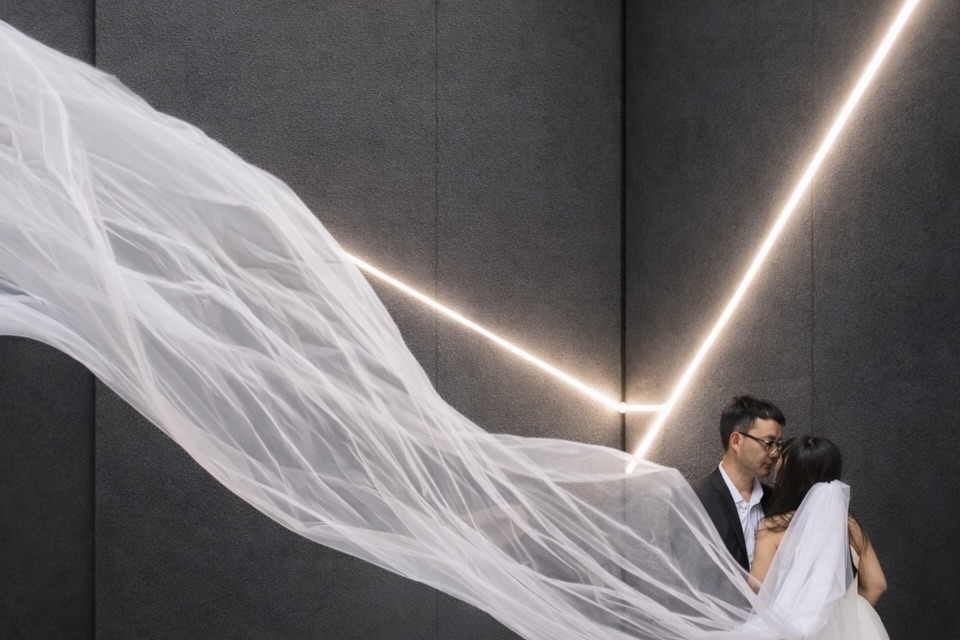 Wedding couple beside a dark wall with white veil fabric sweeping across the frame