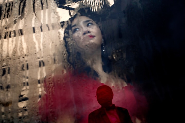 Woman in red seen through glass with a building pattern over her portrait