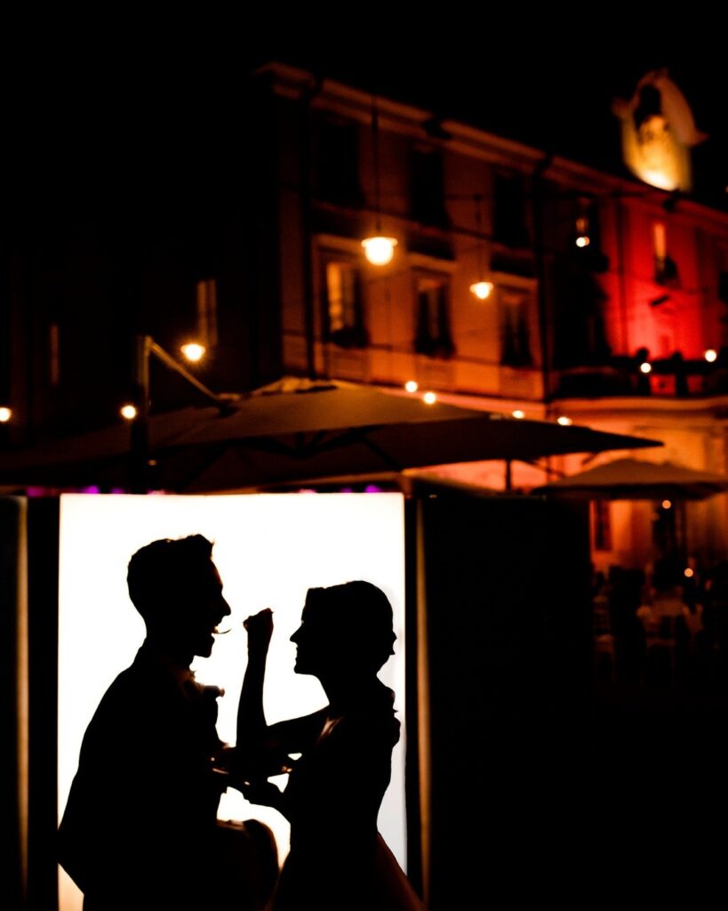 Siluetas de una pareja frente a frente junto a un panel luminoso en una calle nocturna