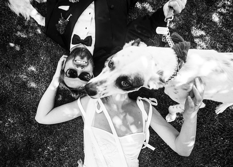 Retrato cenital en blanco y negro de una pareja tumbada en el césped con su perro cerca de la cámara