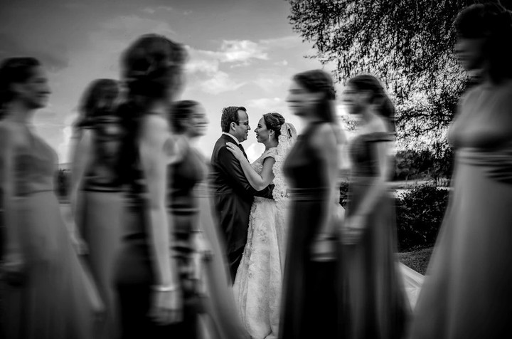 Novios enfocados entre invitados desenfocados que cruzan el primer plano, en blanco y negro