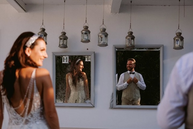 Novia y novio sonriendo al verse reflejados en dos espejos de pared