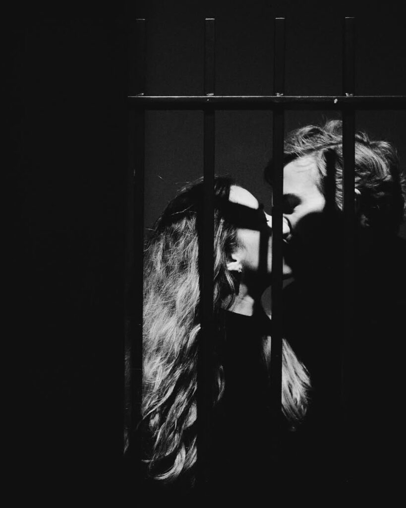 Retrato cercano en blanco y negro de una pareja tras una baranda oscura con franjas de luz