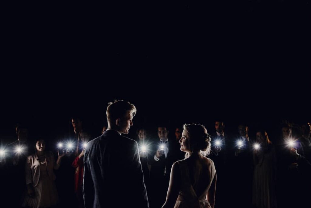 Wedding couple surrounded by guests holding glowing phone lights at night