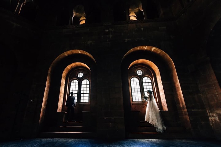 Novia y novio en huecos separados de ventanas arqueadas dentro de un edificio oscuro