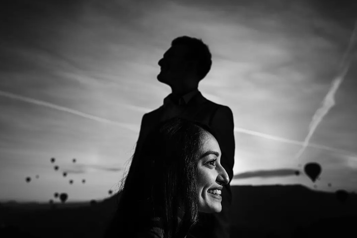 Black and white portrait combining a woman's face, a man's silhouette and distant hot air balloons