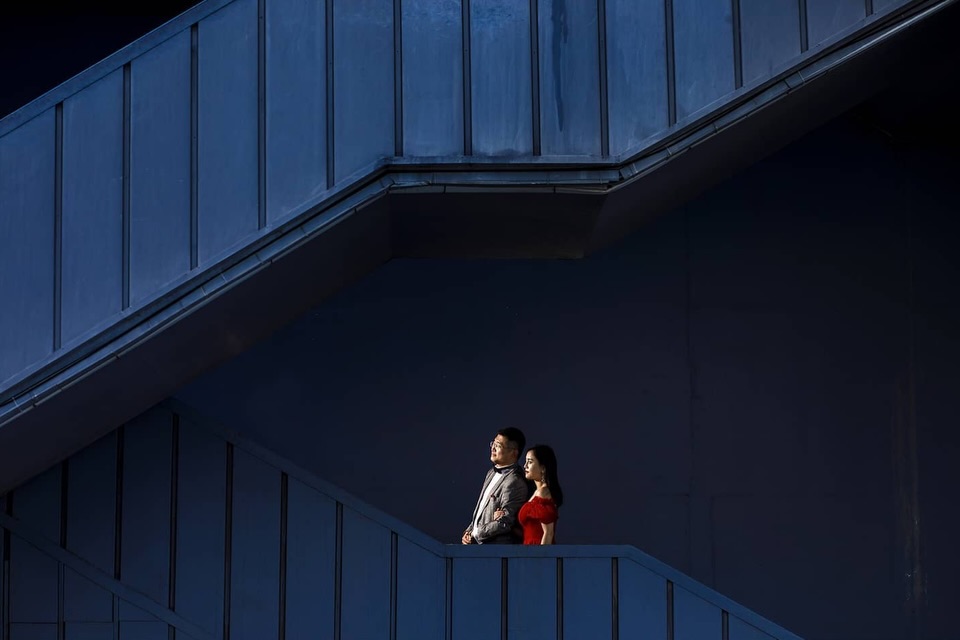 Small couple standing in an opening within deep blue architectural walls