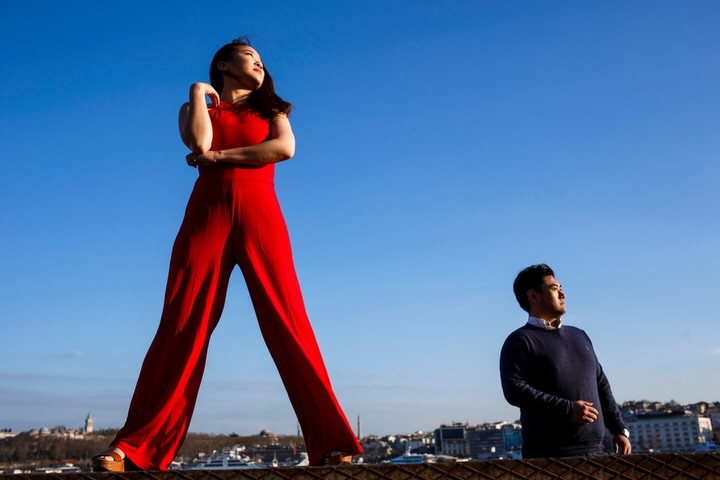 Woman in a red jumpsuit and man standing apart under a large blue sky