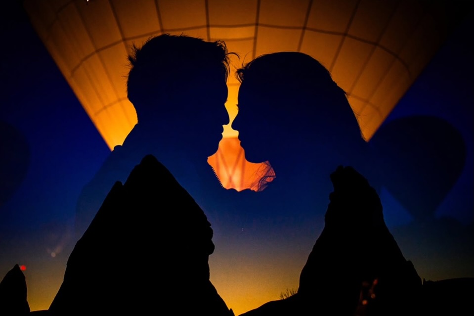 Couple in close silhouette against an orange balloon and deep blue background
