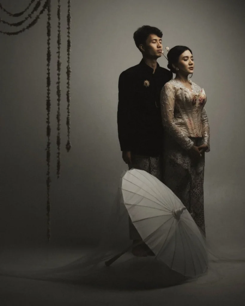 Couple in dark tailoring and a textured dress with a pale parasol