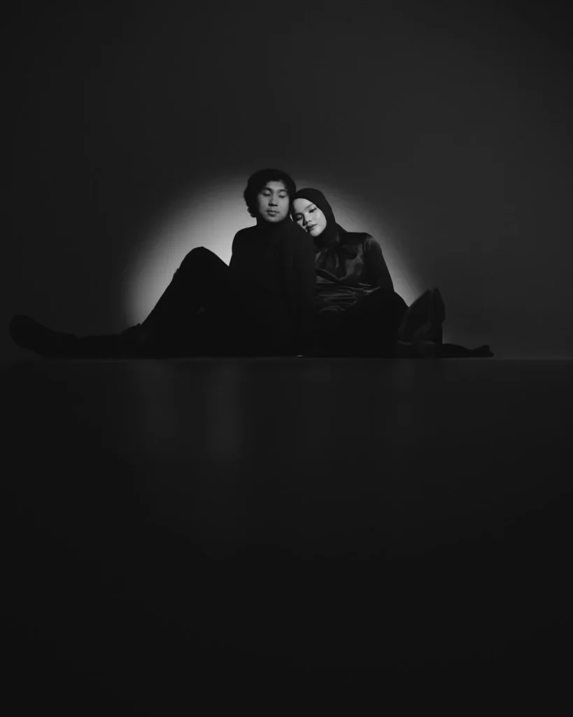 Seated couple against a dark background in a circular patch of light