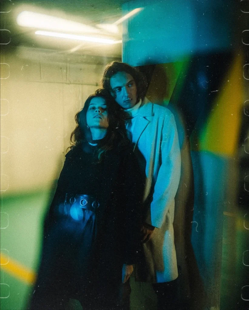 Couple in coats against a wall lit in blue, green and yellow